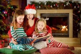 Young mother and her two little daughters reading a book by a Christmas tree in living room